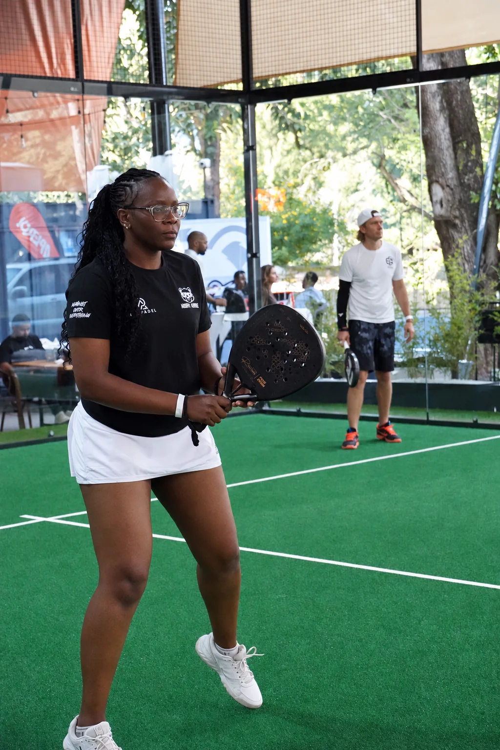 Tonia on court with a padel racket, with other players in the background.